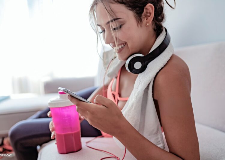 Musica joven fitness con su celular en la mano escogiendo su musica para hacer ejercicio en casa